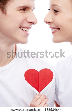 Portrait of a young beautiful couple smiling at each other while girl holding red paper heart