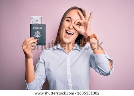 Tourist woman on vacation holding usa passport with dollars banknotes as a travel money with happy face smiling doing ok sign with hand on eye looking through fingers