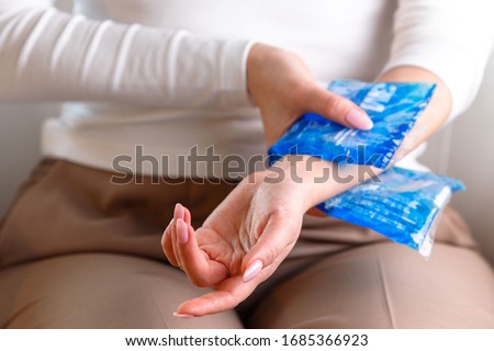 Close up of woman applying cold compress to a her painful wrist caused by prolonged work on the computer, laptop, selective focus on hand. Carpal tunnel syndrome, arthritis, neurological disease. Royalty-Free Stock Photo #1685366923