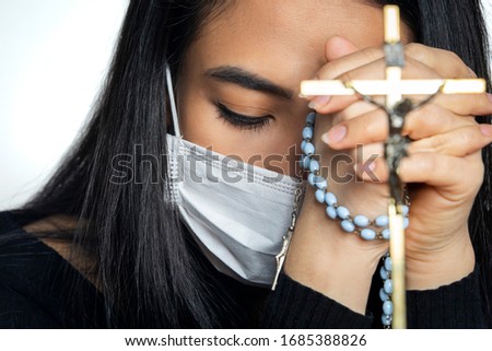 Woman wearing surgical mask praying with rosary. Christian religion hope concept.