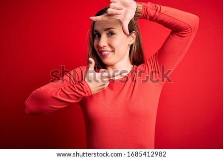 Young beautiful blonde woman wearing casual t-shirt standing over isolated red background smiling making frame with hands and fingers with happy face. Creativity and photography concept.