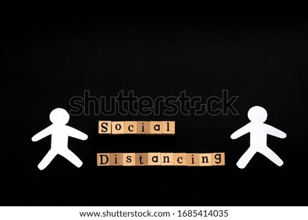 Image of wooden blocks with text say  social distancing between two white human icons isolated on black. Image with copy space.  