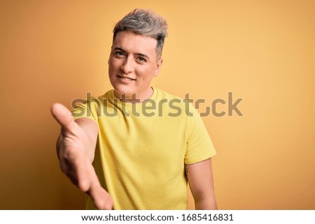 Young handsome modern man wearing yellow shirt over yellow isolated background smiling cheerful offering palm hand giving assistance and acceptance.
