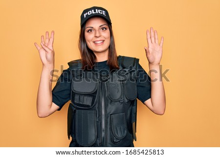 Young beautiful brunette policewoman wearing police uniform bulletproof and cap showing and pointing up with fingers number nine while smiling confident and happy.