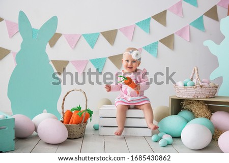 Little beautiful and charming girl sister along with rabbit sitting on the floor or chair in bright blue clothes Easter, eggs, festive mood, emotion and smile surprise holiday celebration