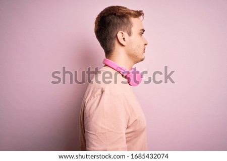 Young handsome redhead man listening to music using headphones over pink background looking to side, relax profile pose with natural face with confident smile.