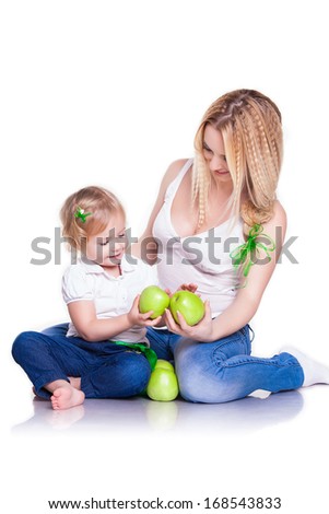 Attractive female with cute baby girl, closeup portrait of young mother and her little daughter with green apples, studio shot, happy family, child care and love concept