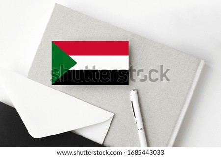 Sudan flag on minimalist letter background. National invitation envelope with white pen and notebook. Communication concept.