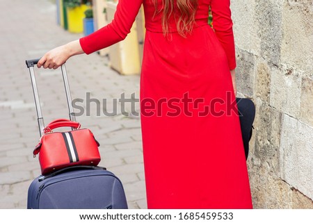 Woman in red dress walks with suitcase on road of city street.