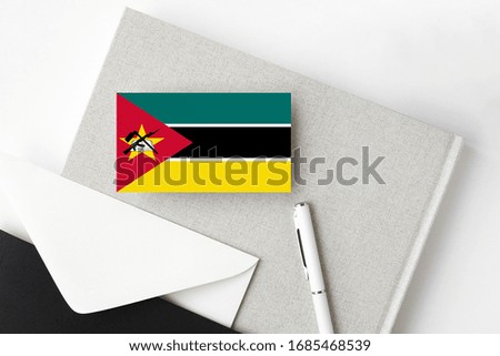 Mozambique flag on minimalist letter background. National invitation envelope with white pen and notebook. Communication concept.