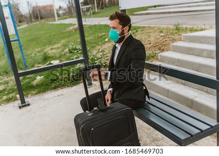Portrait of a man in a suit with a protective medical mask sitting at the bus station waiting for transportation