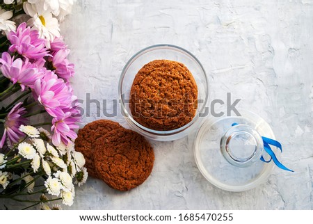 Oatmeal cookies in a glass jar. Bouquet of flowers. Tender woman composition on a gray background Top view.