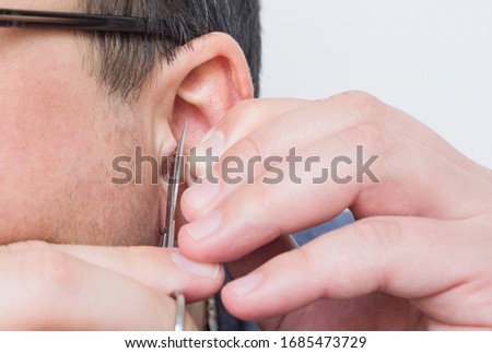 Man removes or cuts his unwanted hair in ears with small scissors at home.