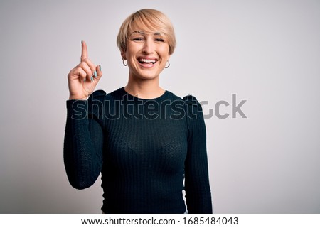 Young beautiful blonde woman with modern short hair hairstyle standing over isolated background pointing finger up with successful idea. Exited and happy. Number one.