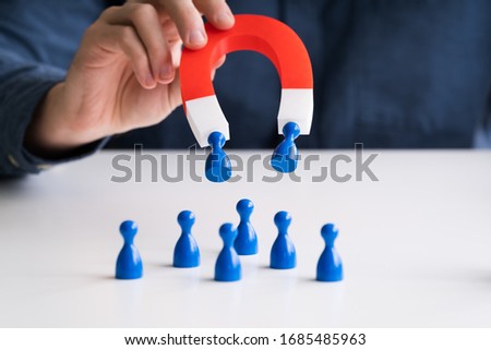 Businessman's Hand Attracting Blue Human Figures Standing In A Row With Horseshoe Magnet