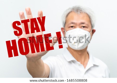 Older man wearing N95 mask holding out his hand with palm out stretch to stop COVID-19 virus with red text STAY HOME overlay - health concept