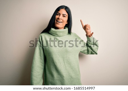 Young beautiful hispanic woman wearing green winter sweater over isolated background pointing finger up with successful idea. Exited and happy. Number one.