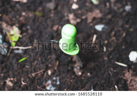 A green handled garden trowel pushed into the soil ready to plant some home grown vegetation, nice detail on the handle itself, and the surrounding soil. Large aperture image emphasising the focus.