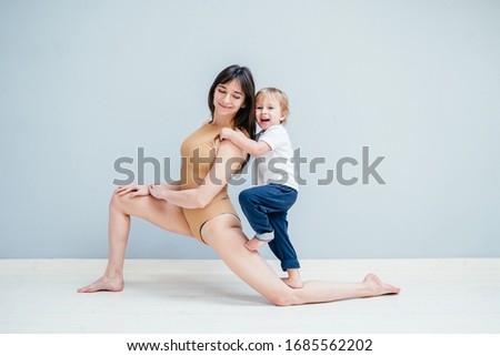 Fitness mother with her 3 years old son. Sports mom with kid doing morning work-out at home. Mum and child do the exercises together, kid climbing on mom, healthy family lifestyle concept.