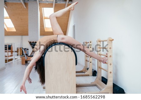Sharming sweden fit woman in beige swimsuit stretching back on a ladder barrel with other pilates equipments on background. Relax, workout,exercising at studio.