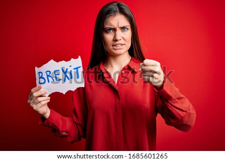 Young beautiful woman with blue eyes holding paper with a message over red background annoyed and frustrated shouting with anger, crazy and yelling with raised hand, anger concept