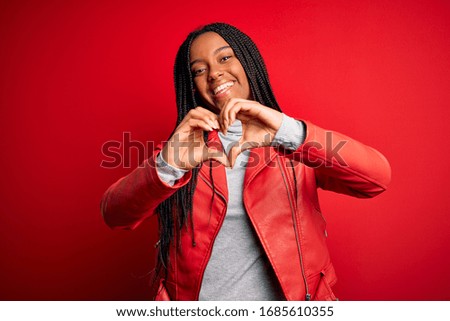 Young african american woman wearing cool fashion leather jacket over red isolated background smiling in love doing heart symbol shape with hands. Romantic concept.
