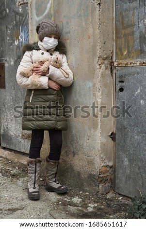 concept of epidemic and quarantine - a girl with a face mask and a cuddly toy alone on the street in the city