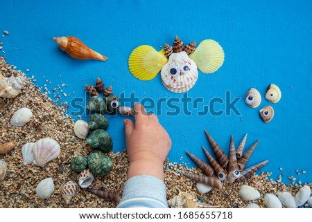 Child's hand playing with sand and sea shells, making art with natural materials