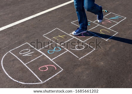 A young man playing hopscotch on asphalt.