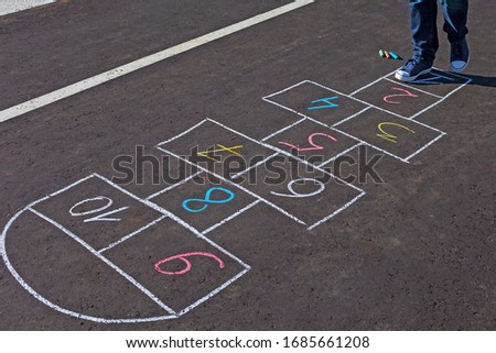 A young man playing hopscotch on asphalt.