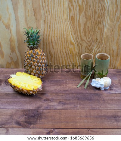 Interior composition of a home on brown wooden table and yellow wall. Handmade spa white elephant candle. Tropical fruit fresh pineapple and cut half. Decorative bamboo glasses from Thailand. 