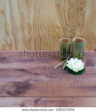 Interior composition of a home on brown wooden table or floor and yellow wall. White lotus spa aroma candle. Decorative bamboo glasses from Thailand. Modern interior background.