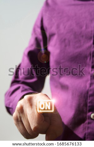 Pressing a virtual On button a right hand of a Caucasian man in a purple shirt, on blurred background