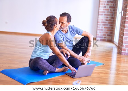 Middle age beautiful sporty couple smiling happy. Sitting on mat kissing using laptop at gym