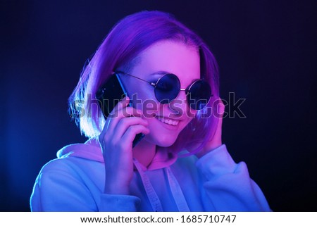 Fashionable young woman in neon light is holding a smartphone. Woman with colored hair, informal. Nightlife. Copy space.