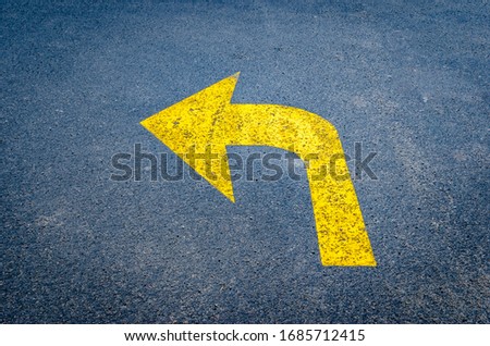 Yellow arrow on black pavement pointing left