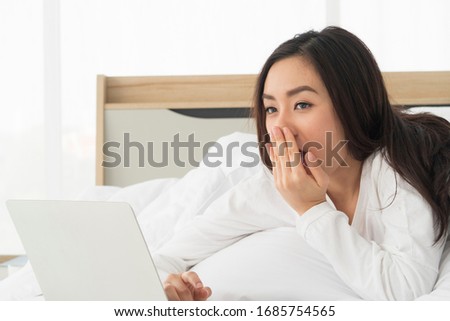 Young beautiful Asian woman using laptop or notebook for working at home in emotional Sleepy while laying on bed in the bedroom. Communication Technology, marketing online, social media concept.