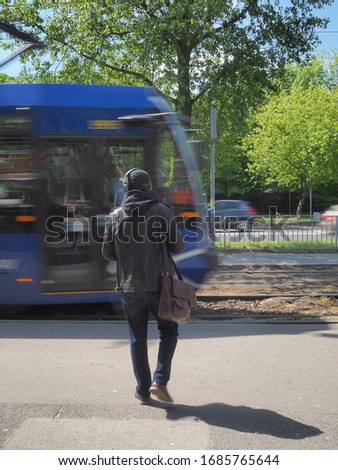 A man in headphones and a baseball cap approaches the oncoming tram