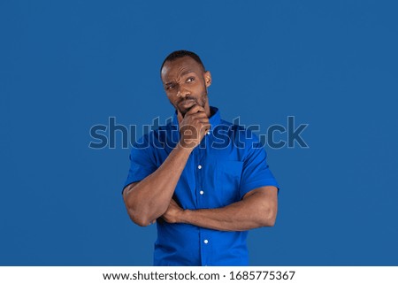 Thinking, dreaming. Monochrome portrait of young african-american man isolated on blue studio background. Beautiful male model. Human emotions, facial expression, sales, ad concept. Youth culture.