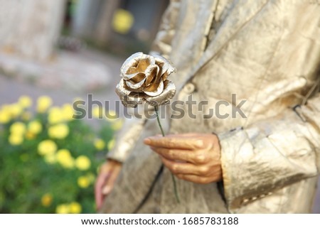 Golden rose as a symbol in the hands of a person painted with gold paint