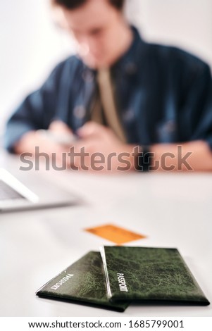 Man texting message while preparing for trip in background, focus on passports in green cases on table