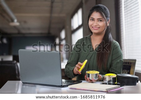 Indian/Asian girl or women eating lunch box, sabji Or sabzi and roti Or chapati in a lunch box. Sitting over office Or college background. Offering food Royalty-Free Stock Photo #1685811976