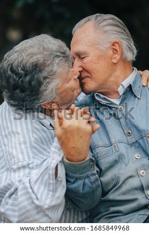 Old couple in a park. Grandparents embracing. Woman in a blue shirt.