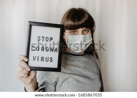 Woman, girl wearing medical mask and holding white board with text stop coronavirus, COVID-19, white background. Covid-19 ( SARS-CoV-2 ) spread around the world. Impact of pandemic virus.
