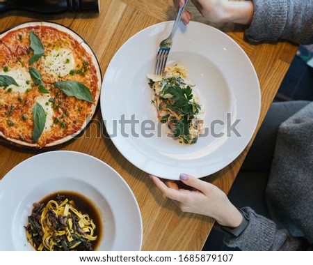
Business lunch, a girl at a table with Italian dishes, pizza, soup, salad, with a mobile phone in her hands