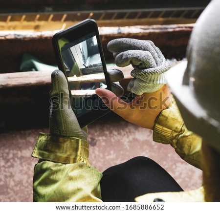 Architect holding a smartphone on construction site. young construction worker is using mobile phone on site. Construction worker with building plans and cellphone. Focus on mobile. warm vivid filter.