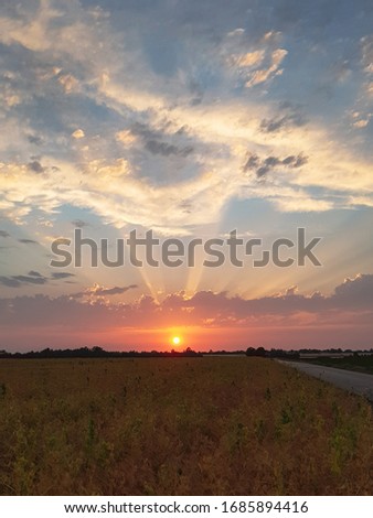 Vertical picture of a colorful sunset on a field just outside of Euskirchen, NRW, Germany. The sky is tinted in colors ranging vom gold, to red, to orange to blue with nicely illuminated clouds. 