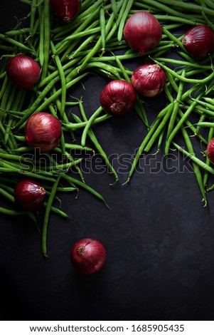 Green beans and red onions scattered across a dark grey background.  Portrait flat lay or top view for perfect background with space for text.