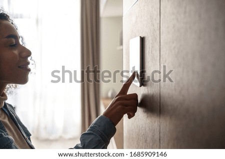 Young african woman using smart home touch screen ai technology connected appliances device on wall monitoring energy security heating system digital control in apartment. Smart home concept. Closeup Royalty-Free Stock Photo #1685909146