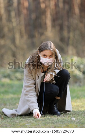 young woman in protective mask listening to the ground with stethoscope in the park. selective focus. copy space.